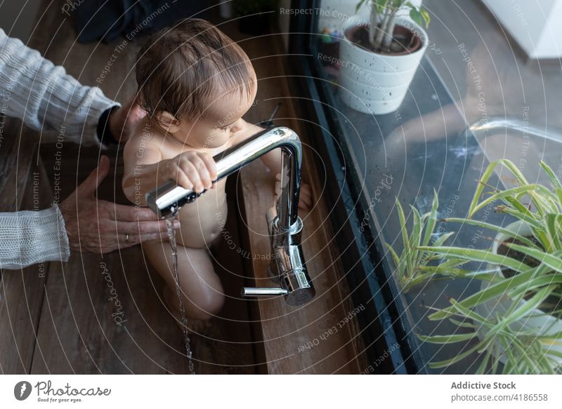 Crop-Vater badet Baby im Waschbecken zu Hause Bad Waschen bezaubernd Freude spielen Wasser Küche Kleinkind nackt Eltern Mann Zusammensein Elternschaft