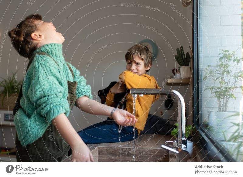 Vergnügte Kinder spielen in der Küche in der Nähe der Spüle Geschwisterkind Wasser Waschbecken Zusammensein Spaß haben Freude sorgenfrei heimwärts Wochenende