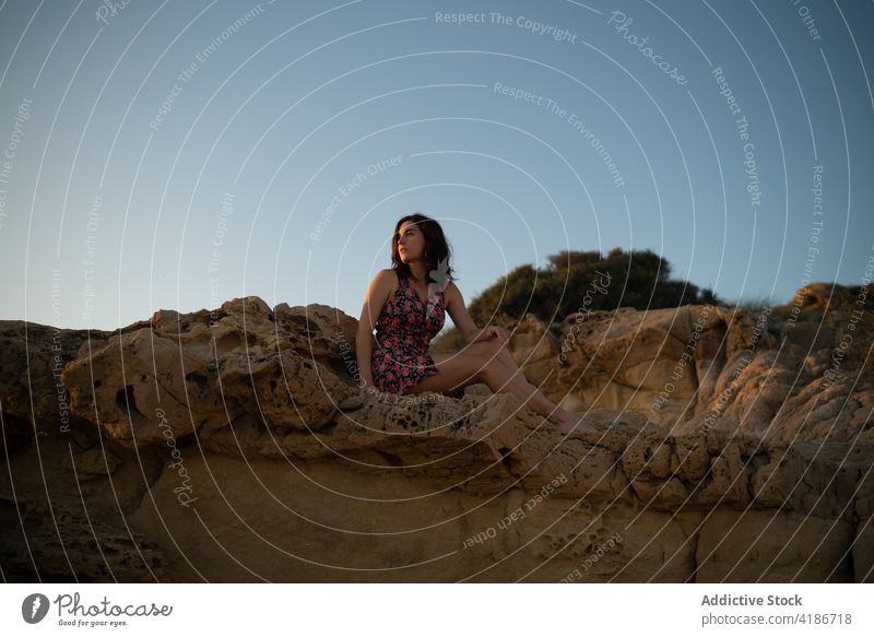 Frau in einem Kleid auf einem Felsen sitzend an einem Sommertag Natur schön Stein Schönheit Lifestyle Glück Mode im Freien Strand jung Sonnenuntergang Behaarung