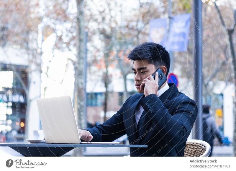 Fröhlicher ethnischer Geschäftsmann arbeitet in einem Cafe Café Arbeit abgelegen multitask Projekt Lächeln Laptop Smartphone beschäftigt männlich asiatisch Mann