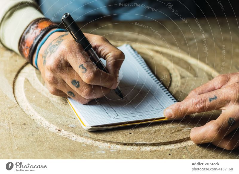 Crop Holzarbeiter Zeichnung Skizze in Notizbuch Tischlerin zeichnen Schreinerei Notebook Tiefgang Zimmerer reif Mann Tischlerarbeit männlich Lebensmitte Tattoo