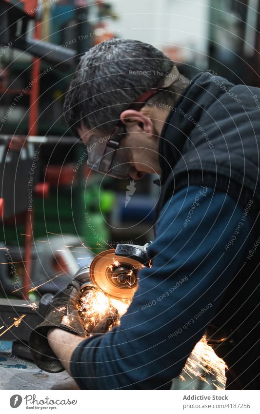 Aufmerksamer Mechaniker beim Schneiden von Metall mit einer elektrischen Schleifmaschine in der Werkstatt Mann geschnitten Metallbearbeitung Funken Reparatur