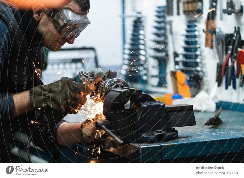 Aufmerksamer Mechaniker beim Schneiden von Metall mit einer elektrischen Schleifmaschine in der Werkstatt Mann geschnitten Metallbearbeitung Funken Reparatur