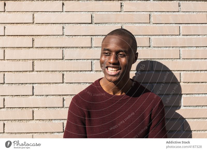 Glücklicher junger Afroamerikaner in der Nähe der Quartiermauer stehend Mann lässig Stil maskulin nachdenken Schatten Backsteinwand Stadt allein schwarz