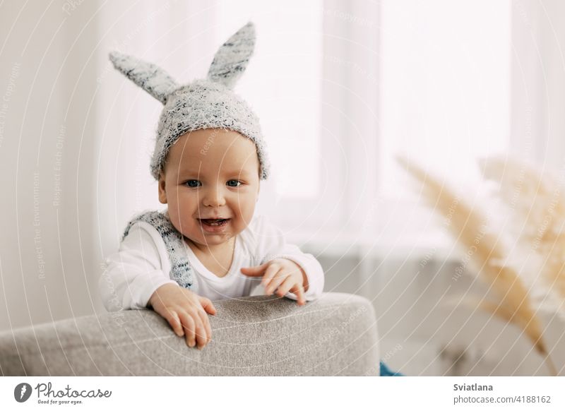 Kind in lustigen Osterhase Kostüm sitzt auf einem Stuhl und lacht Baby Kaninchen Anzug Ostereier Spiel Sitzen Spielzeug Bett Innenbereich Lachen schlafen
