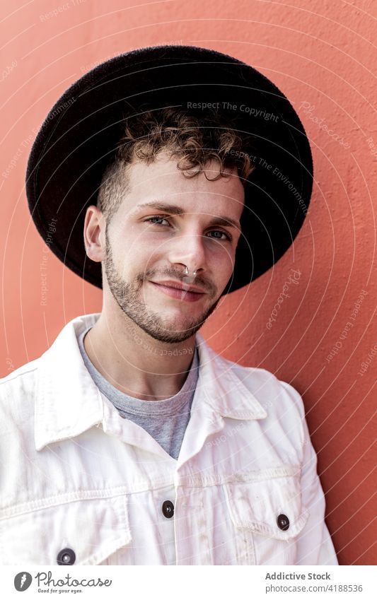 Glücklicher junger Mann lächelnd vor rotem Hintergrund Lächeln selbstbewusst Inhalt Stil trendy Persönlichkeit ausrichten Hut sich[Akk] entspannen Straße cool