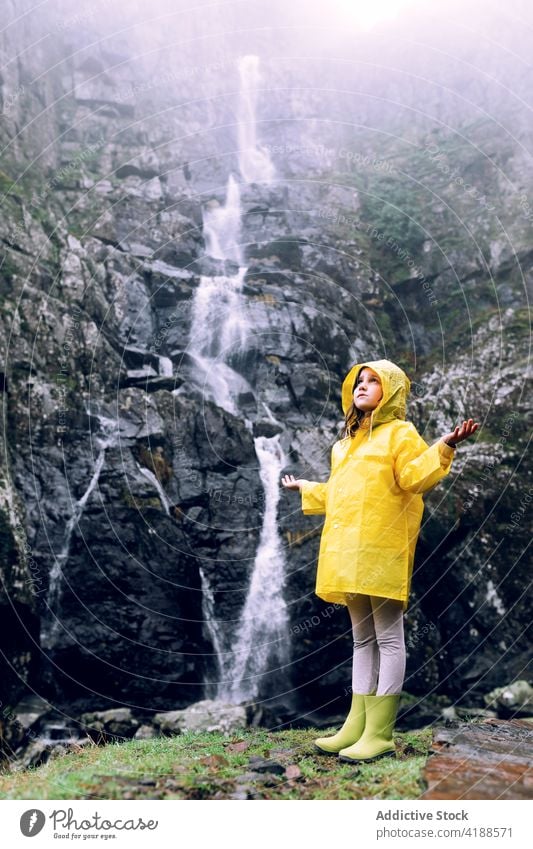 Mädchen in gelbem Regenmantel vor einem Wasserfall in den Bergen Berge u. Gebirge Arme hochgezogen Tourismus Hochland Natur Fernweh reisen verträumt Kaskade