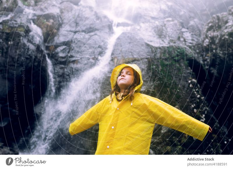 Mädchen in gelbem Regenmantel vor einem Wasserfall in den Bergen Berge u. Gebirge Arme hochgezogen Tourismus Hochland Natur Fernweh reisen verträumt Kaskade