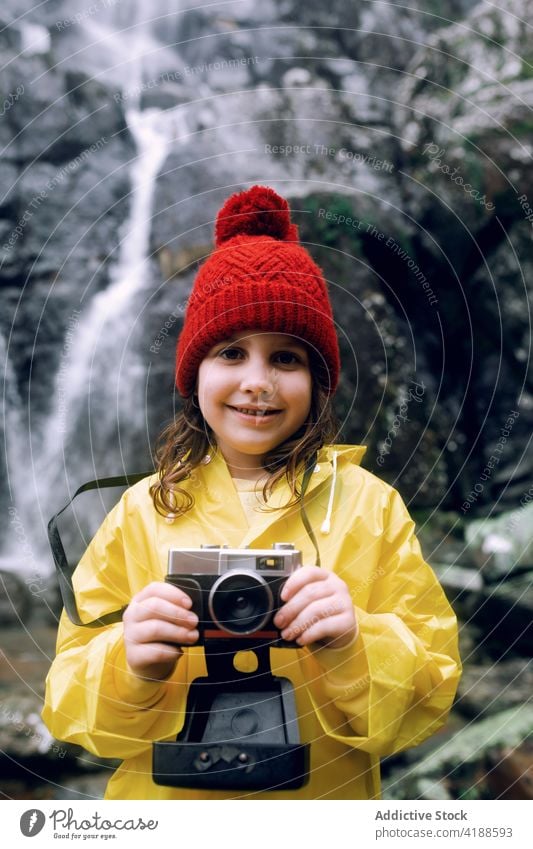 Glücklicher Teenager, der ein Foto mit der Kamera gegen einen Wasserfall auf einem Berg macht fotografieren Fotoapparat Berge u. Gebirge Natur Gedächtnis