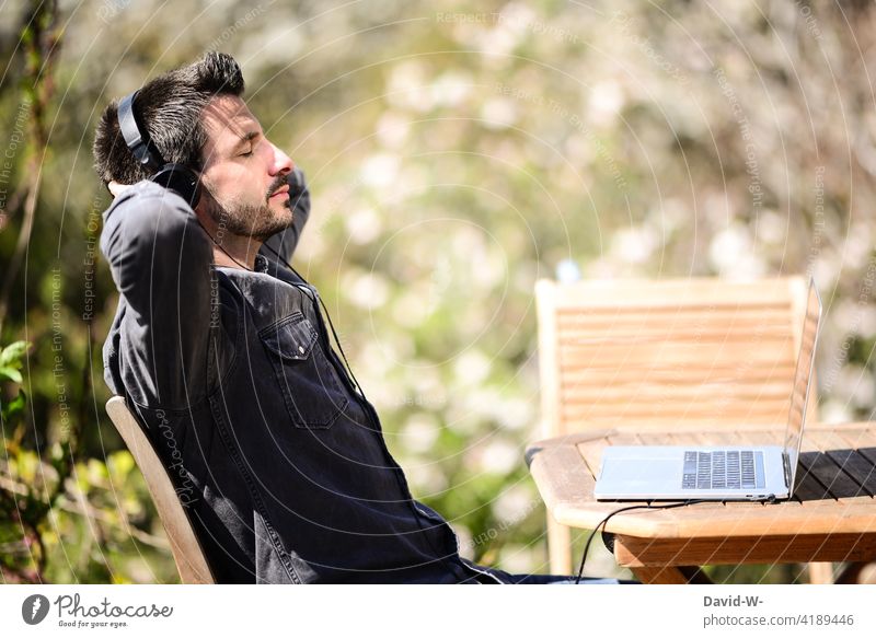Mann mit Kopfhörer und Laptop hört Musik streamen hören genießen entspannung draußen relaxen Erholung