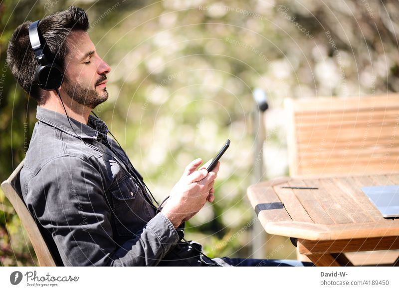 Mann hört Musik über sein Handy - Enstpannung streamen hören Kopfhörer entspannung genießen Auszeit chillen Natur Schönes Wetter Lifestyle
