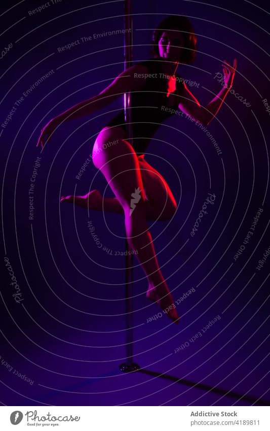 Anmutige Tänzerin tanzt an einer Stange im Neonlicht Tanzen Mast Tastkopf Beine gekreuzt Körper Augen geschlossen erotisch neonfarbig Frau Arm angehoben