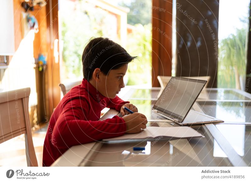 Junge macht Hausaufgaben am Tisch mit Laptop Kind schreiben Notebook sorgsam lernen Schuljunge Pupille Handschrift Gerät klug Apparatur Bildung Aufgabe Wissen