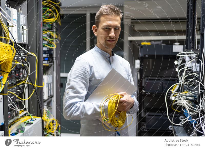 Lächelnder Techniker mit Laptop und Spule elektrischer Drähte Mann Kabel Draht elektronisch Maschinenbau Dienst Einrichtung männlich Netzwerk Server Daten