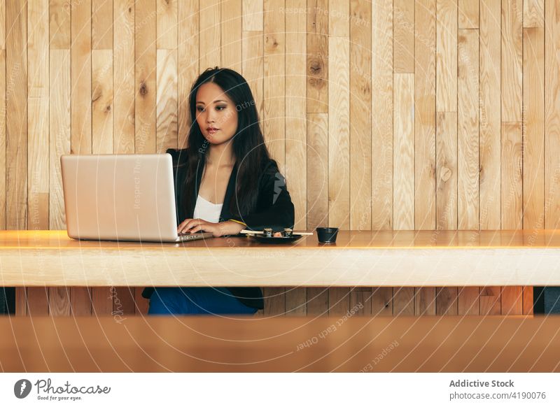 Ethnische Geschäftsfrau isst Sushi und arbeitet am Laptop in einem Café Arbeit essen rollen Projekt Unternehmer abgelegen Frau asiatisch ethnisch Tisch