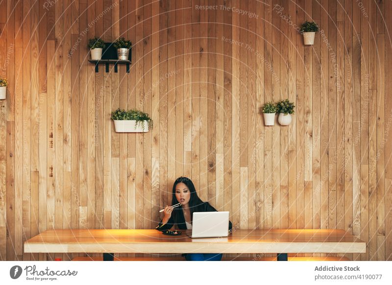 Ethnische Geschäftsfrau isst Sushi und arbeitet am Laptop in einem Café Arbeit essen rollen Projekt Unternehmer abgelegen Frau asiatisch ethnisch Tisch