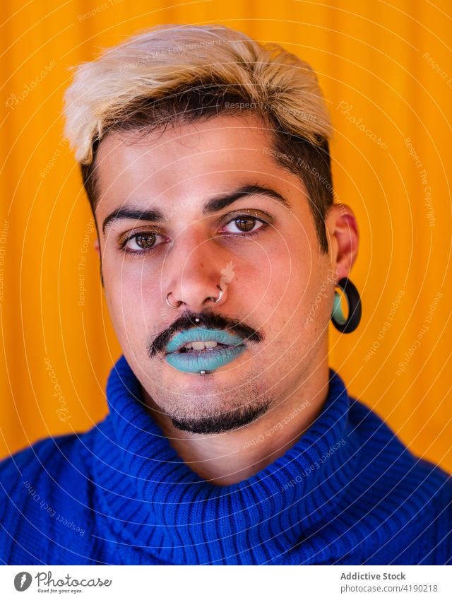 Stilvoller Mann mit Make-up schaut in die Kamera androgyn trendy Model alternativ Bekleidung Gesicht männlich blau Lippe Lippenstift emotionslos Outfit gelb