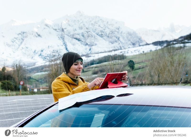 Frau benutzt Tablet in der Nähe des Autos in winterlichem Berggelände PKW Autoreise Landkarte Tablette benutzend Berge u. Gebirge Winter Hochland Inhalt