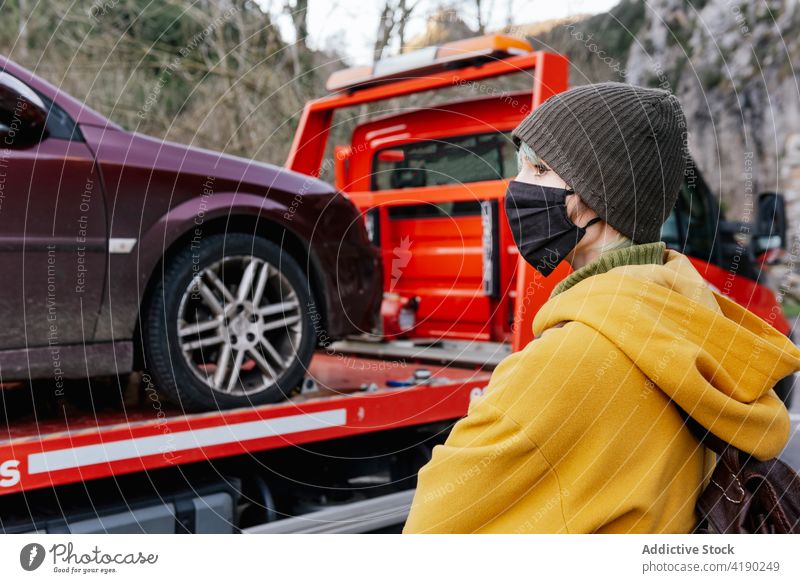 Frau mit Maske steht in der Nähe eines abgeschleppten Autos schleppen Lastwagen PKW Panne Oberbekleidung Mundschutz Coronavirus Problematik Fahrer Verkehr