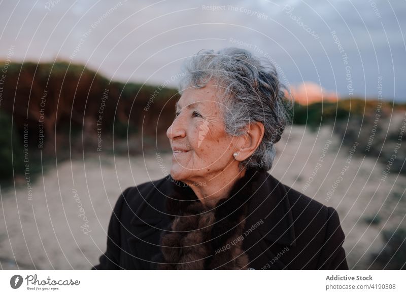 Positiv gestimmte ältere Frau lächelt, während sie sich am Abend am sandigen Meeresufer ausruht Lächeln sich[Akk] entspannen Strand Tourist Glück Porträt