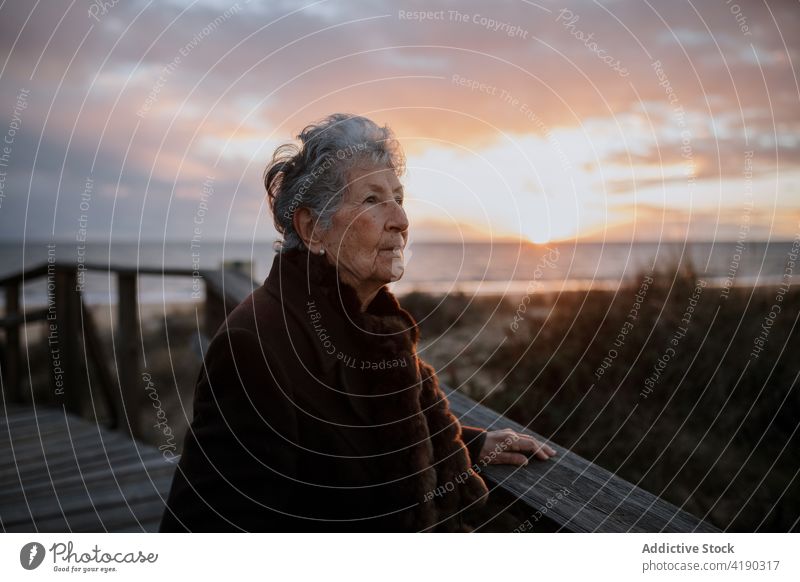 Ältere Dame bewundert den Sonnenuntergang über dem Meer von der Strandpromenade aus Frau bewundern Meereslandschaft Reisender genießen Natur Urlaub reisen MEER