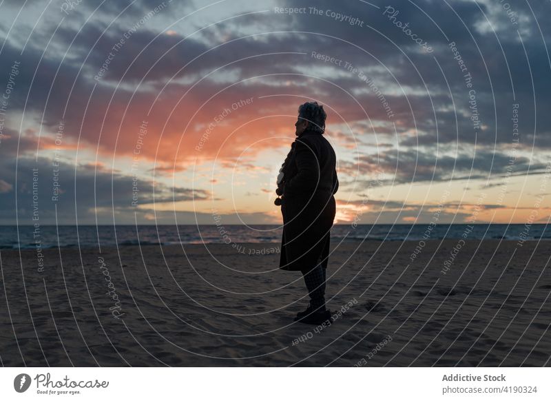 Anonyme ruhige ältere Frau, die sich bei Sonnenuntergang am Strand erholt bewundern MEER Windstille genießen sich[Akk] entspannen allein Natur Landschaft