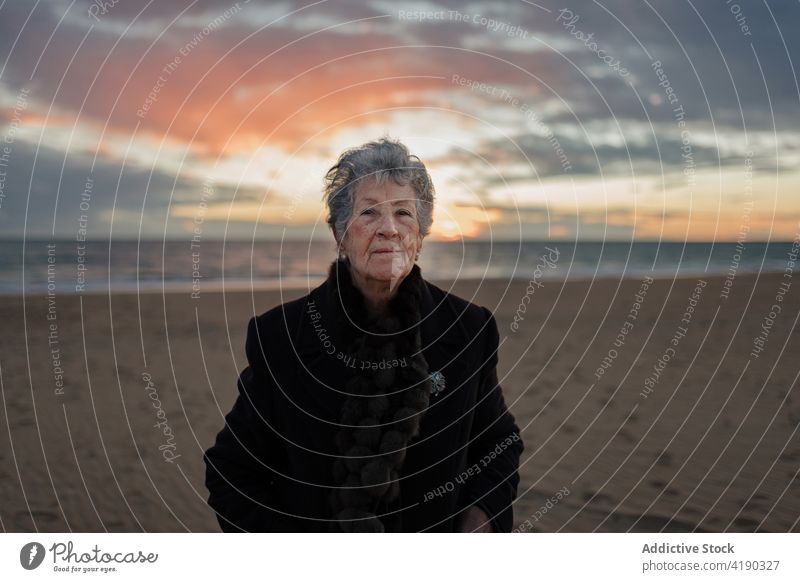 Ruhige ältere Frau, die sich bei Sonnenuntergang am sandigen Meeresufer erholt bewundern MEER Strand Windstille genießen sich[Akk] entspannen allein Natur