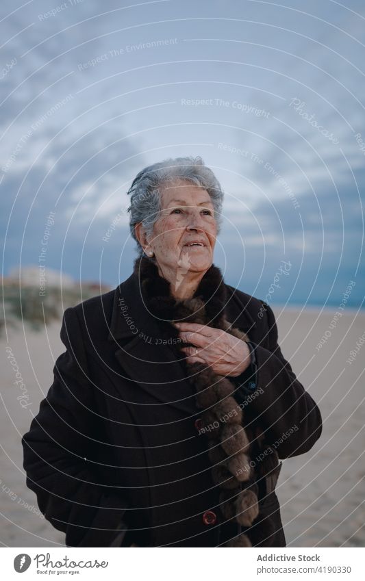 Ältere Frau ruht sich abends am sandigen Meeresufer aus sich[Akk] entspannen Strand Tourist Porträt Feiertag Küste ruhen wolkig Abend Himmel älter graues Haar
