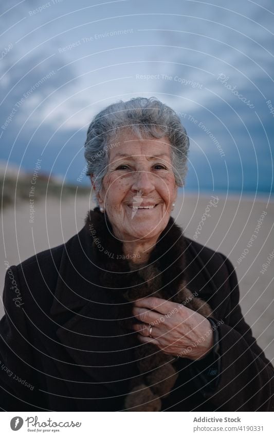 Positiv gestimmte ältere Frau lächelt, während sie sich am Abend am sandigen Meeresufer ausruht Lächeln sich[Akk] entspannen Strand Tourist Glück Porträt
