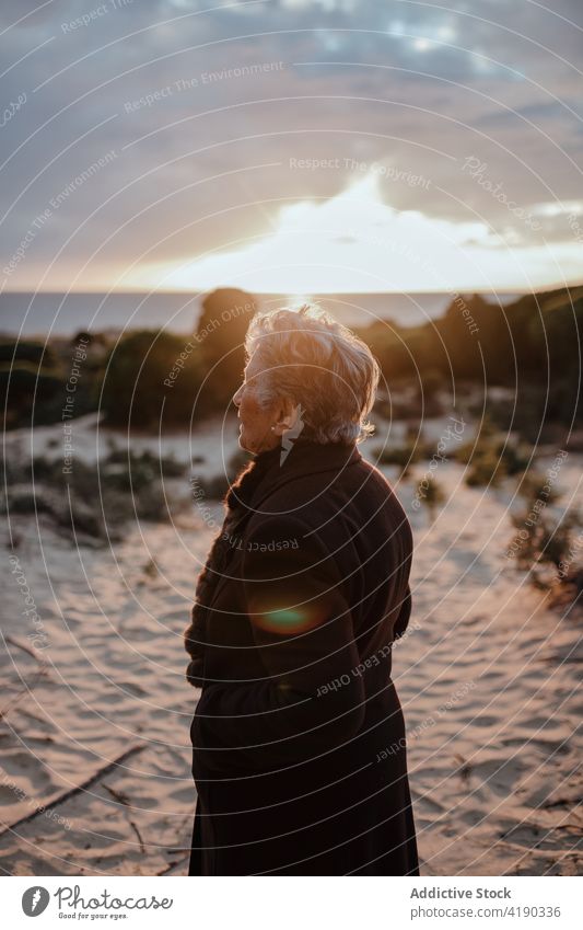 Ältere Frau ruht sich abends am sandigen Meeresufer aus sich[Akk] entspannen Strand Tourist Porträt Feiertag Küste ruhen wolkig Abend Himmel älter graues Haar