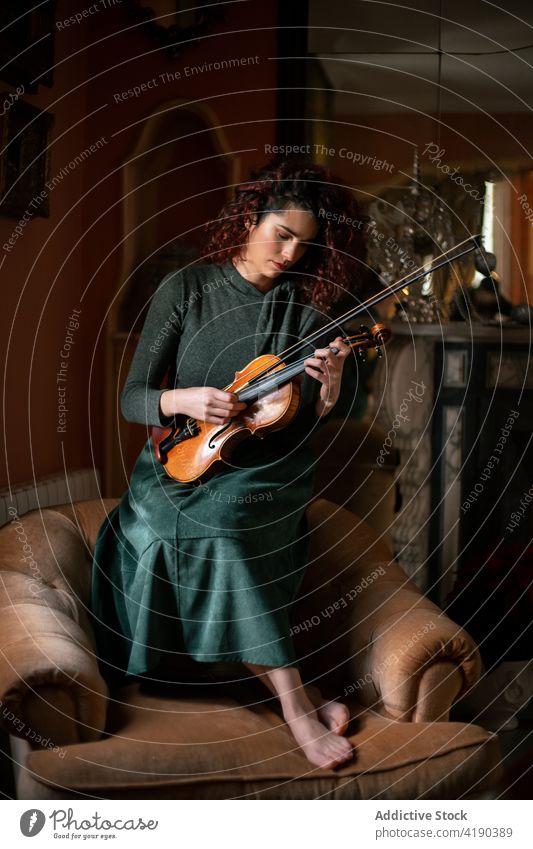 Talentierte Geigerin spielt im Zimmer Frau Musiker klassisch spielen Armsessel Raum Probe Instrument altehrwürdig Melodie Klang Kunst Fokus Inspiration Dame