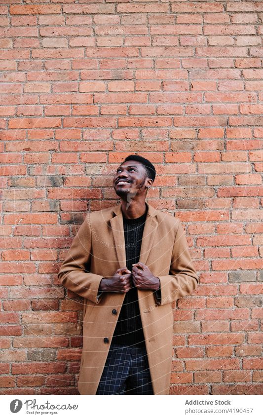 Stilvoller schwarzer Mann, der auf der Straße an einer Backsteinmauer steht Afroamerikaner modern trendy selbstbewusst urban Lifestyle Außenseite Mantel