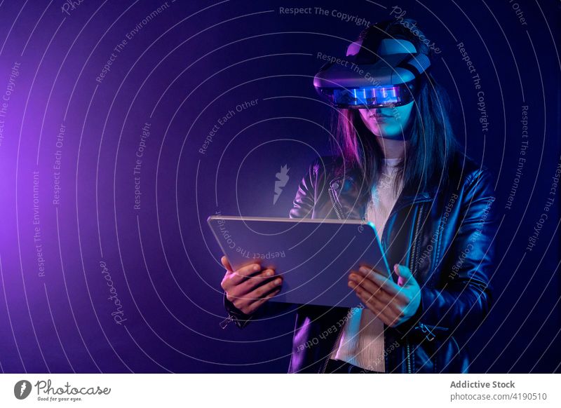 Unerkennbare Frau mit VR-Brille surft auf einem Tablet Schutzbrille Headset neonfarbig Virtuelle Realität Tablette Cyberspace Erfahrung Technik & Technologie