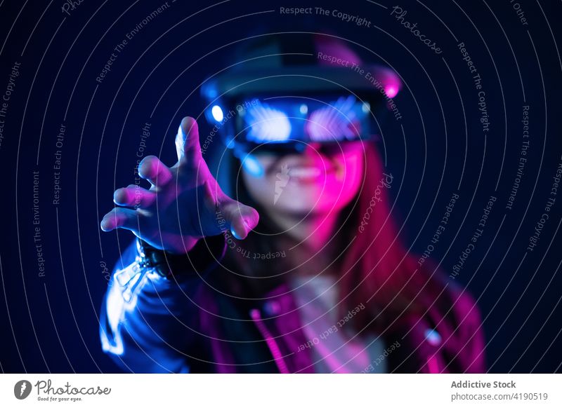 Anonyme Frau mit VR-Brille im Neonlicht Schutzbrille Headset neonfarbig Licht ausdehnen Virtuelle Realität Technik & Technologie Cyberspace leuchten simulieren