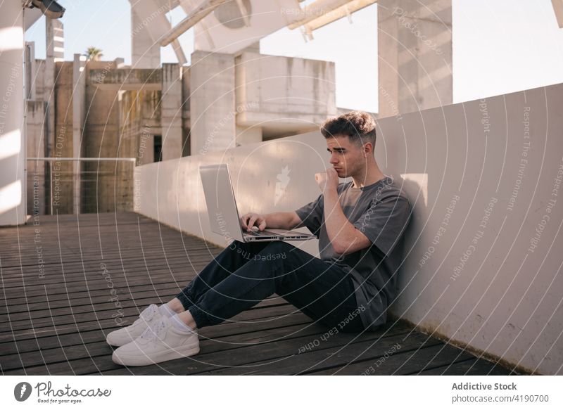 Konzentrierter Mann mit Laptop bei der Online-Arbeit auf dem Dach freiberuflich abgelegen Konzentration Dachterrasse beschäftigt selbständig männlich jung