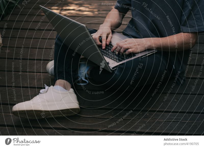 Anonymer Mann sitzt auf der Promenade und tippt auf einem Netbook während eines Fernstudiums Tippen Laptop Schüler Entfernung Lektion Internet Feiertag