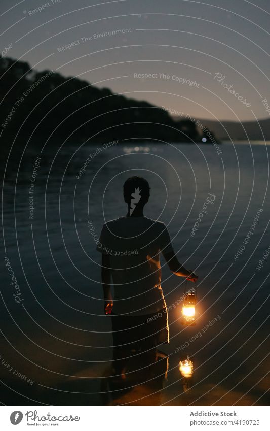 Anonymer Reisender mit Laterne bewundert See gegen Berg bei Nacht bewundern Reittier Natur Landschaft Himmel Mann glänzend Rippeln Wasser Silhouette Tourist