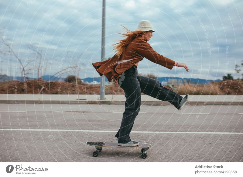 Aktive junge Frau fährt Skateboard in der Natur Mitfahrgelegenheit Longboard Straße Landschaft Aktivität Trick Hobby Subkultur üben aktiv Bein angehoben trendy