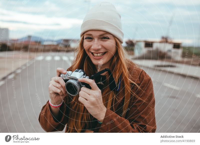 Fröhliche junge Fotografin lächelt, während sie auf der Straße auf dem Land steht Frau fotografieren Lächeln positiv Tourist Ausflug Landschaft altehrwürdig