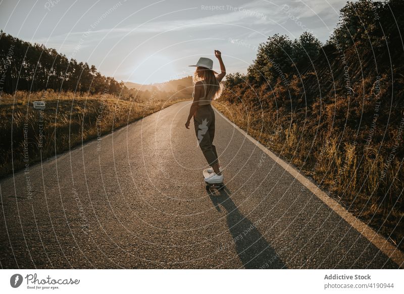 Stilvolle Frau beim Schlittschuhlaufen auf leerer Landstraße Skater Mitfahrgelegenheit Cruiser Straße ländlich aktiv Energie Skateboard Gleichgewicht Fahrbahn