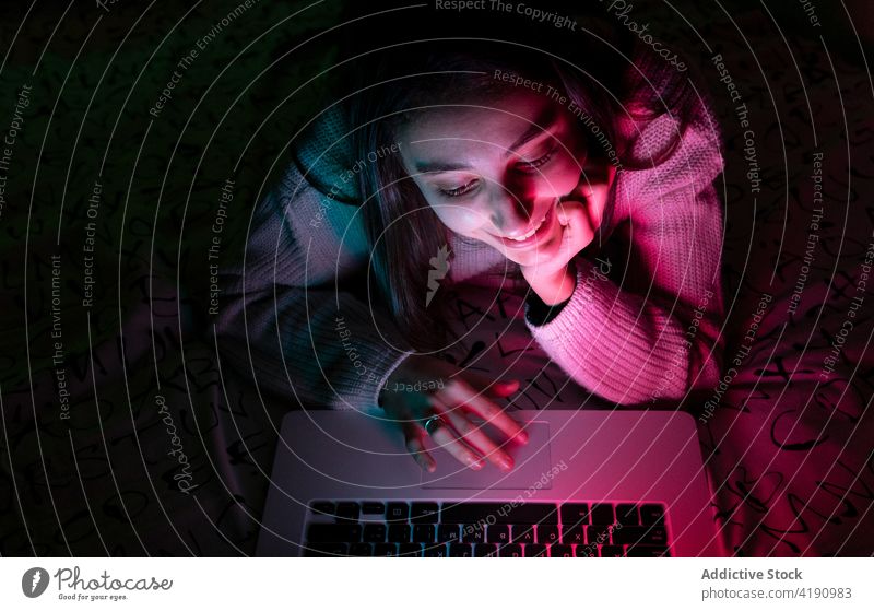 Junges Mädchen surft auf Laptop im Zimmer leuchten heimwärts Browsen Lächeln Teenager Gerät Surfen Raum online heiter Apparatur Internet Schlafzimmer Pullover