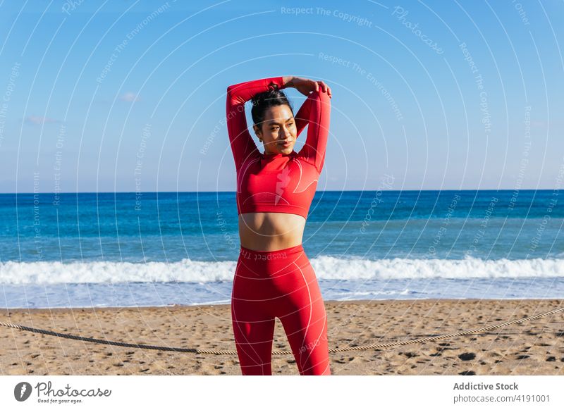 Positive junge hispanische Frau, die sich vor dem Training am sandigen Meeresufer aufwärmt Aufwärmen Dehnung Strand selbstsicher Athlet Gesundheit Wellness