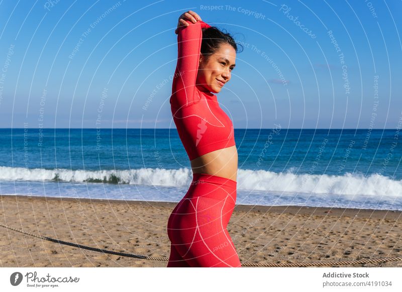 Positive junge hispanische Frau, die sich vor dem Training am sandigen Meeresufer aufwärmt Aufwärmen Dehnung Strand selbstsicher Athlet Gesundheit Wellness