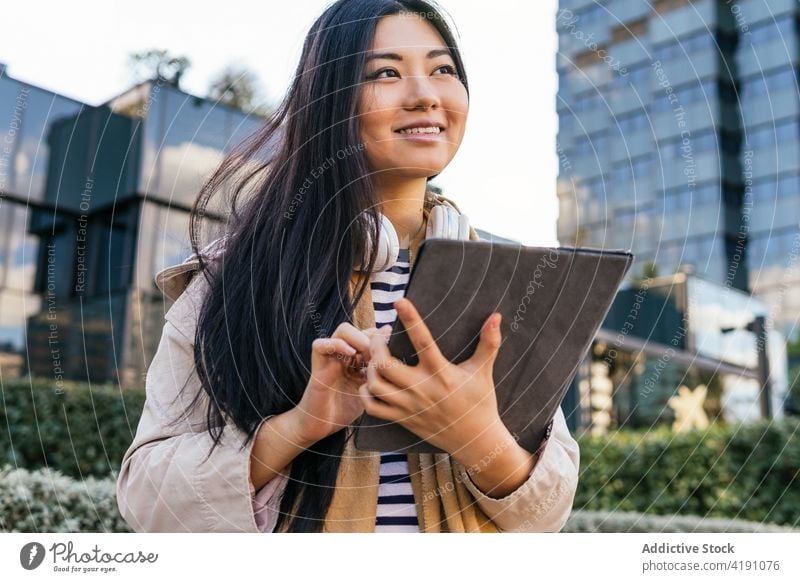 Positive ethnische Frau benutzt Tablette auf der Straße positiv benutzend zuschauen digital Anschluss Suche online Browsen Apparatur Lächeln heiter Surfen