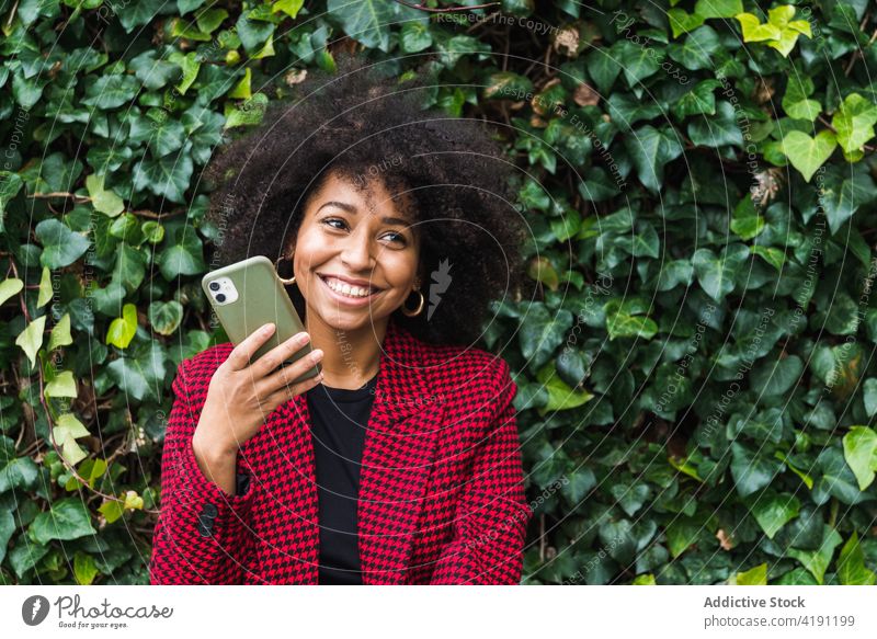 Lächelnde schwarze Frau, die mit einem Smartphone spricht heiter Großstadt ethnisch Afroamerikaner Bank Gerät Apparatur Inhalt Telefon benutzend Glück