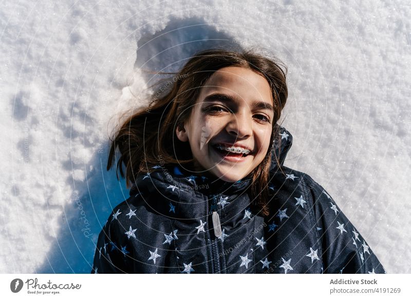 Fröhliches Mädchen im Schnee liegend im Winter Lügen sorgenfrei heiter Teenager Zahnspange offen Lächeln Jacke warm Glück kalt Inhalt Freude Oberbekleidung
