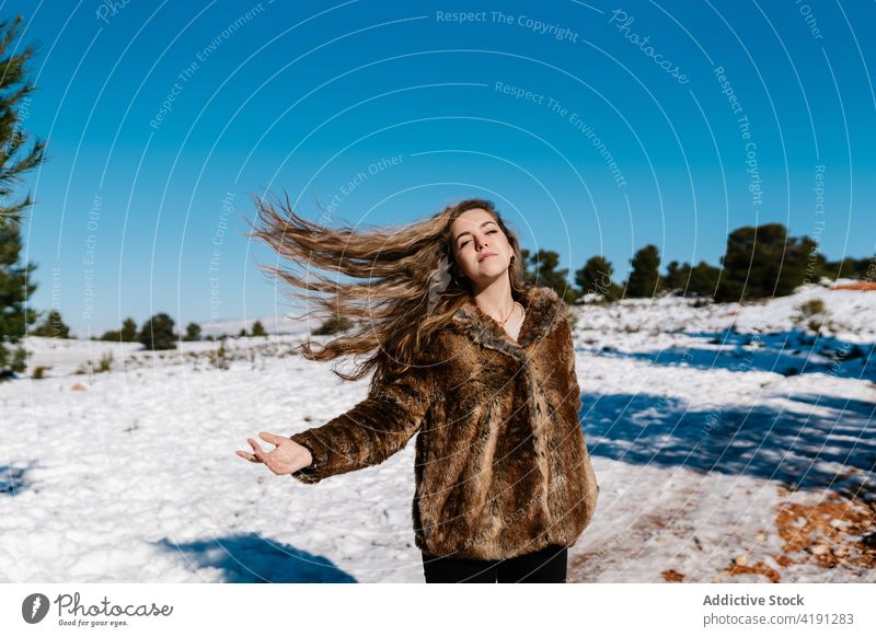 Unbekümmerte Frau spielt mit Haaren im Winterwald sorgenfrei fliegendes Haar wellenförmiges Haar Wiese Wald Schnee sonnig genießen Freiheit Fell Mantel warm