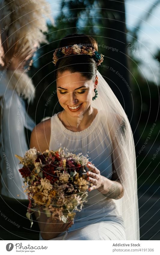 Fröhliche Braut mit Blumenstrauß im Garten hochzeitlich heiter charmant Hochzeit weißes Kleid Jungvermählter Frau Sommer ausgefallen Veranstaltung elegant