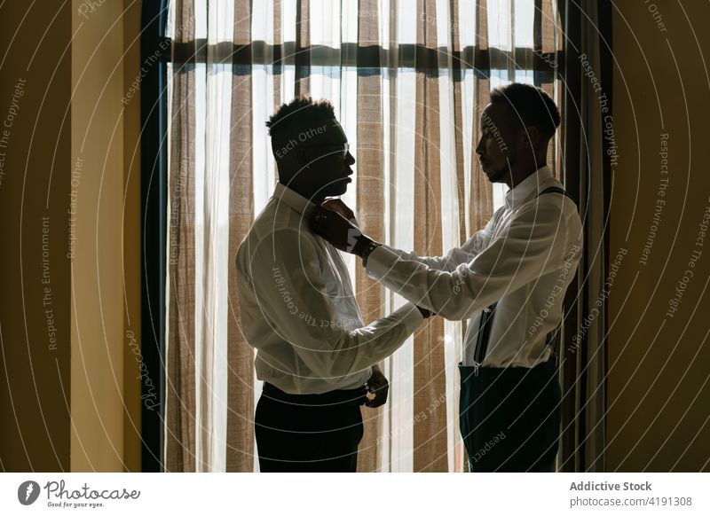 Ethnische Brüder in stilvollen Outfits im Zimmer am Hochzeitstag striegeln ausrichten Fliege Bruder Trauzeuge Hilfsbereitschaft Freund Jungvermählter Verlobter