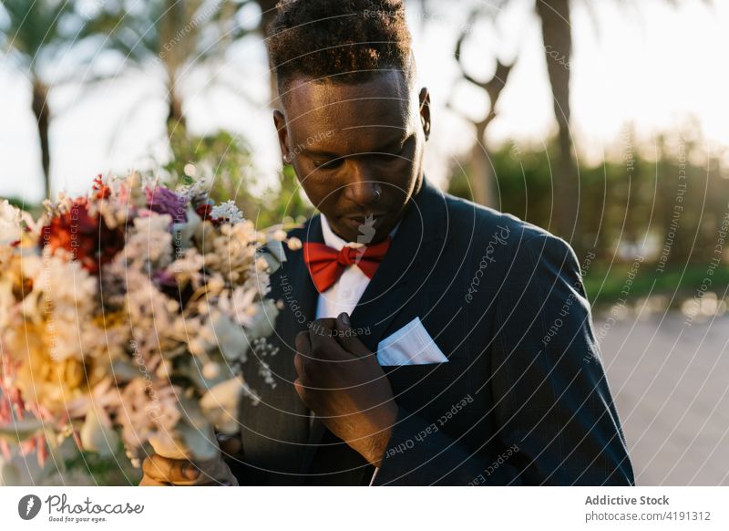 Stilvoller schwarzer Bräutigam mit Blumen im Garten striegeln Blumenstrauß ausrichten Jungvermählter elegant Anzug Hochzeit männlich Mann Afroamerikaner